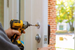 Man Repairing The Doorknob. Closeup Of Worker's Hands Installing New Door Locker