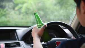 Man Driving A Car While Holding A Bottle Of Beer. Driving Under